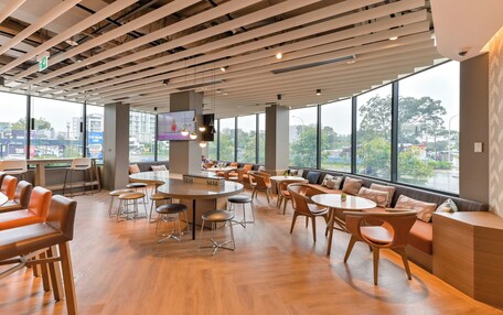 A modern indoor space with wooden flooring, round tables, and orange seating.