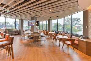 A modern indoor space with wooden flooring, round tables, and orange seating. - Holiday Inn Express Sydney Airport by IHG (Mascot)