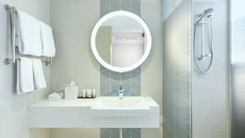 Een moderne badkamer met een witte wasbak, een ronde spiegel en een douche.
