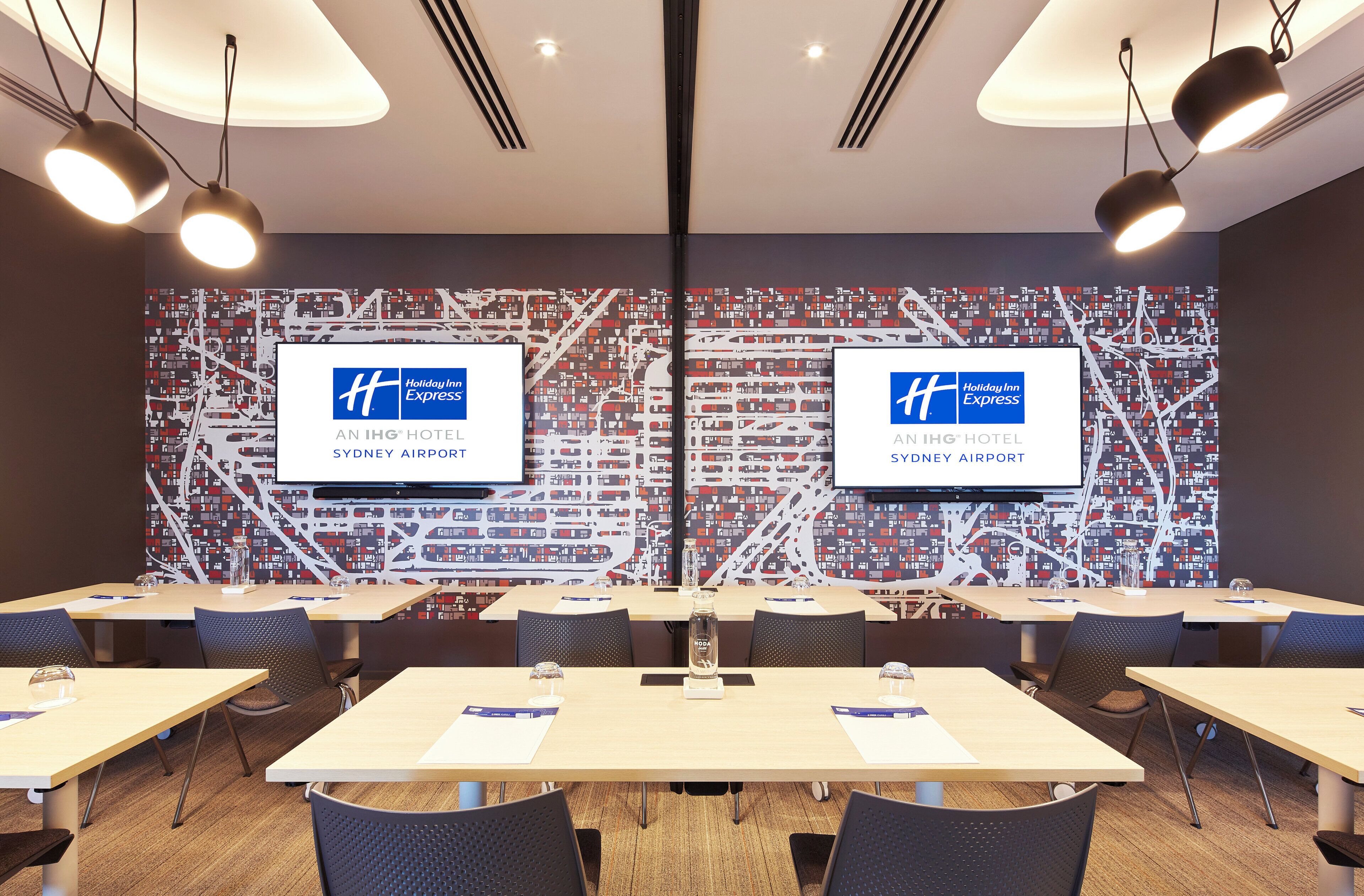 Une salle de conférence dotée d’un grand écran affichant le logo de Holiday Inn Express, de plusieurs tables et de chaises.
