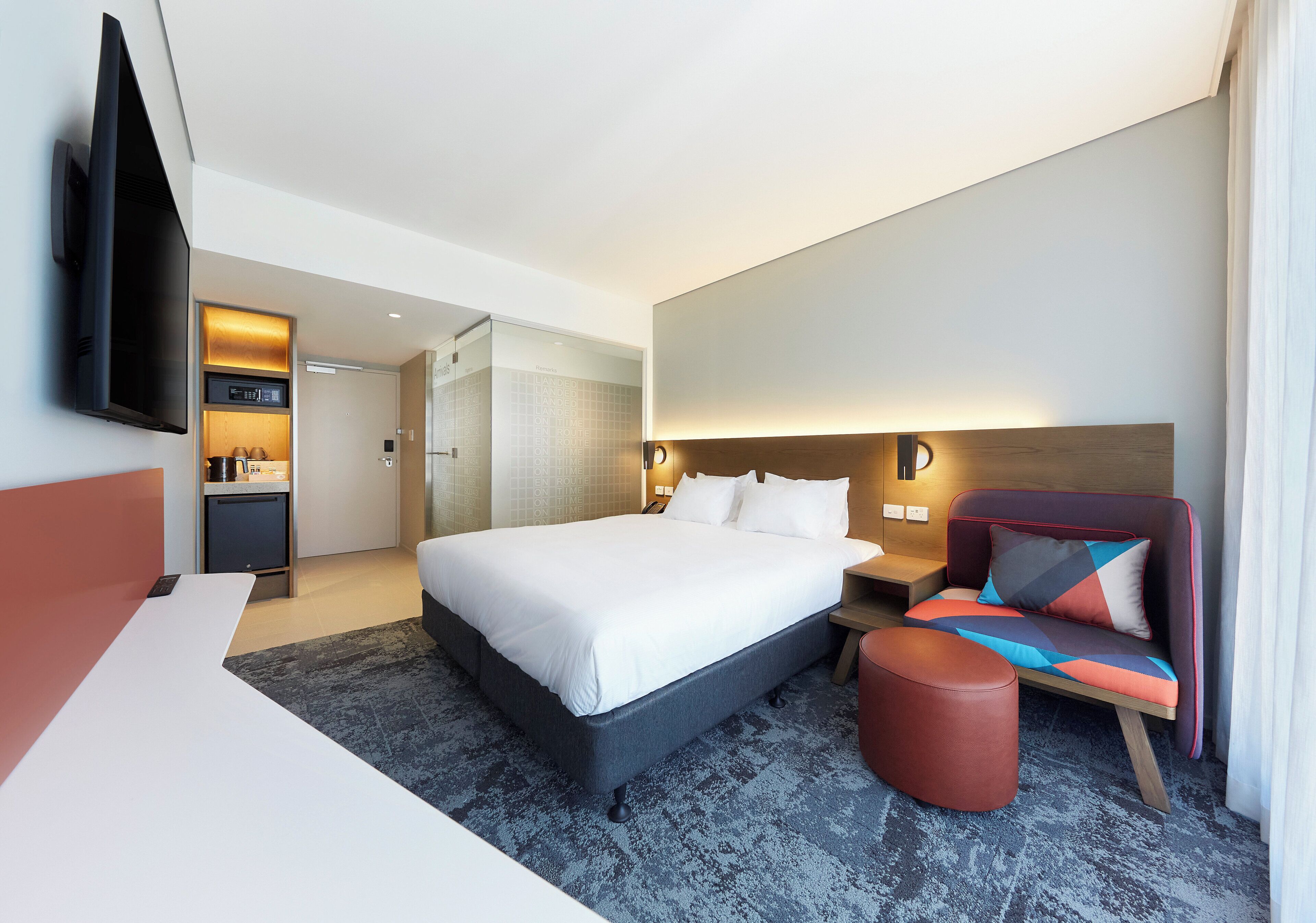 A hotel room with a bed, a TV, a desk, a chair, and a small table.