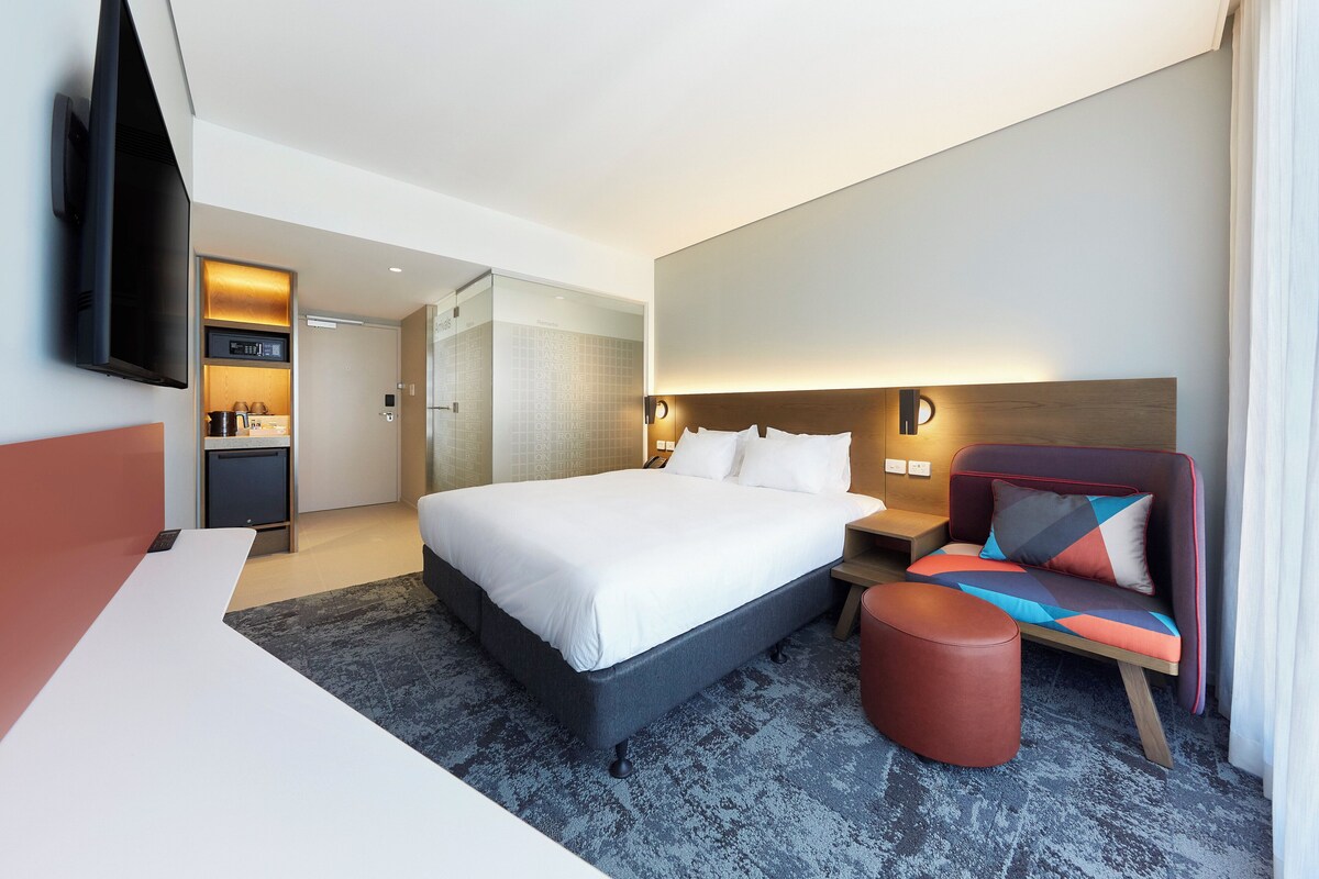 Een hotelkamer met een bed, een televisie, een bureau, een stoel en een klein tafeltje.