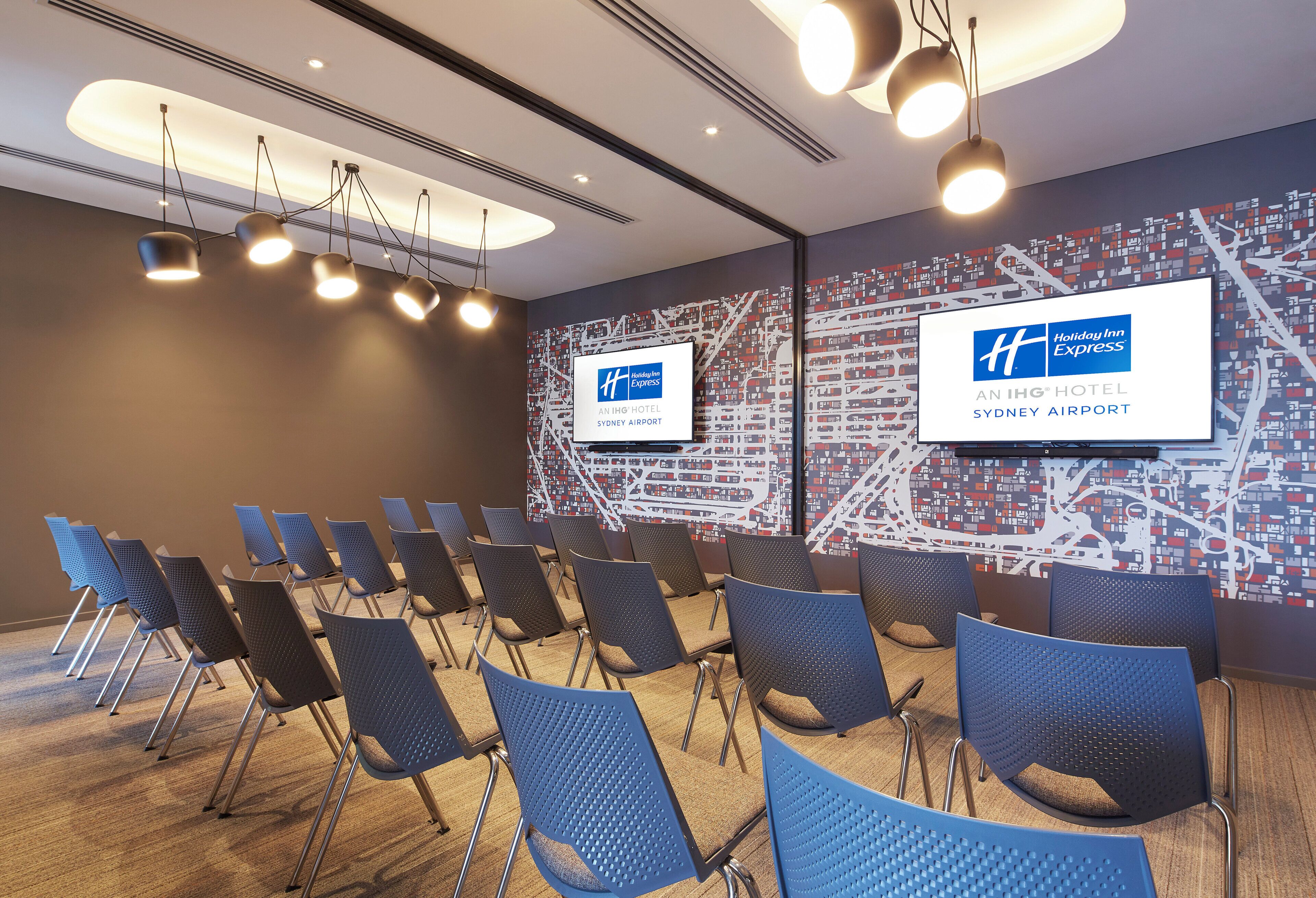 A conference room with rows of chairs, a map wall, and ceiling lights.