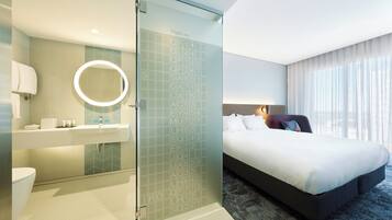Habitación de hotel con cama, baño con espejo y puerta de vidrio con números de vuelo.
