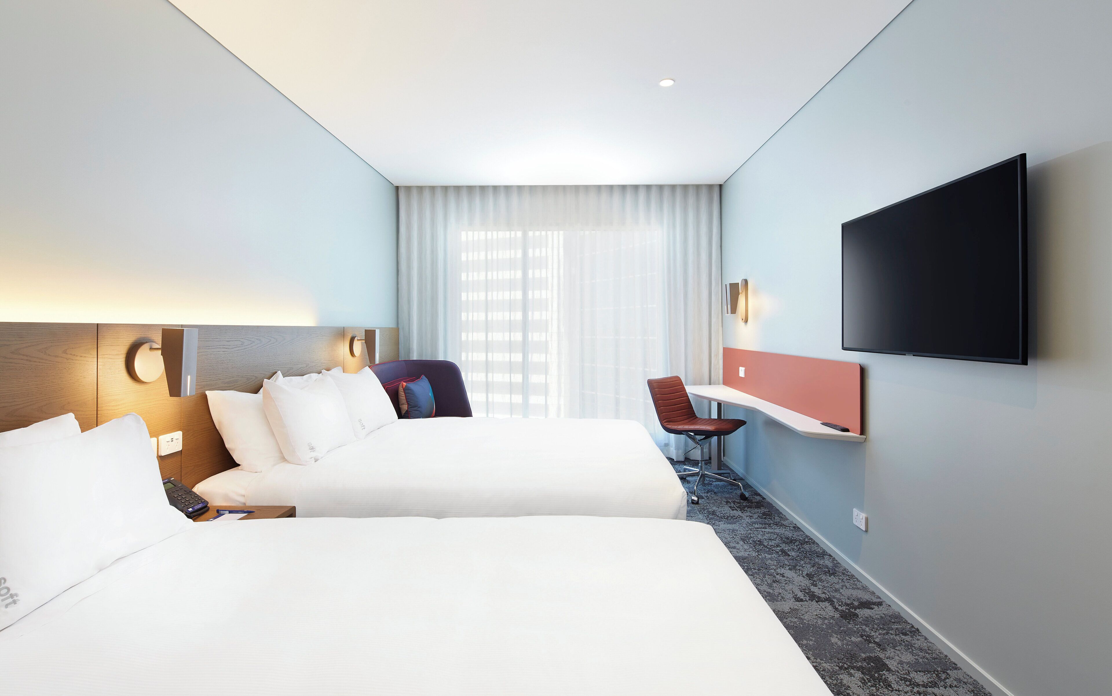 A hotel room with a large bed, a desk, a chair, a TV, and a window with curtains.