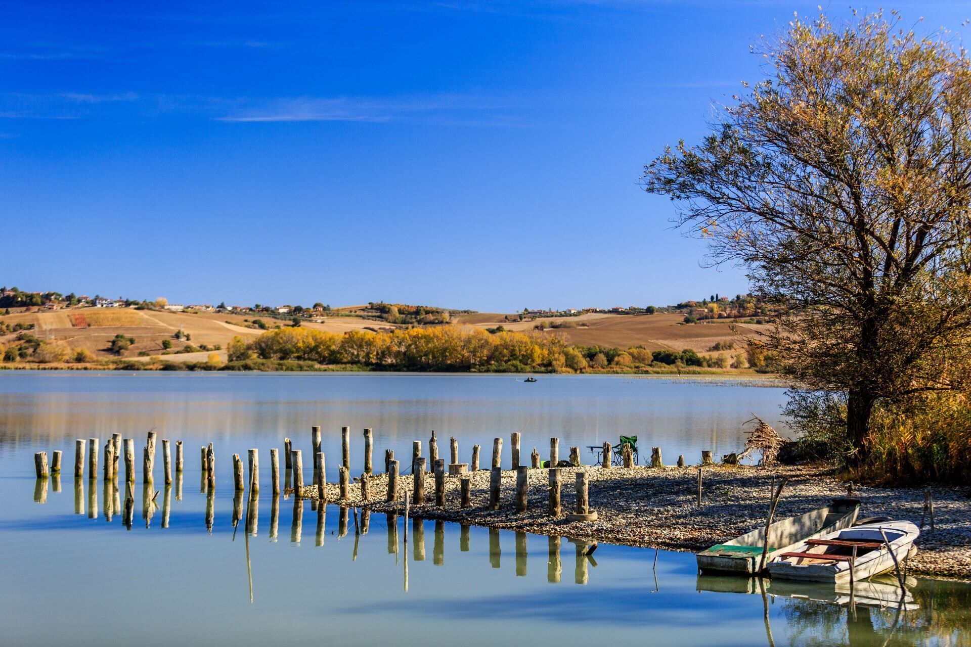 A calm lake with a dock and a boat, surrounded by hills and sparse vegetation.