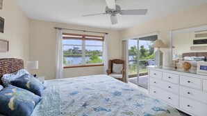 Un dormitorio con cama, una silla, cómoda, ventilador de techo y vista a un lago por la ventana.