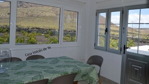 A dining area with a table set for two, large windows with a view of a rocky landscape, and a door with a metal gate. - House overlooking the volcano with garden, solarium, terrace and barbecue (Ye)