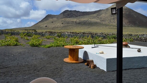 A terrace with a view of a mountain, a wooden table, and a stone wall. - House overlooking the volcano with garden, solarium, terrace and barbecue (Ye)