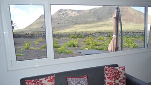A room with a large window overlooking a garden with plants and a mountain. There is a gray sofa with patterned cushions. - House overlooking the volcano with garden, solarium, terrace and barbecue (Ye)