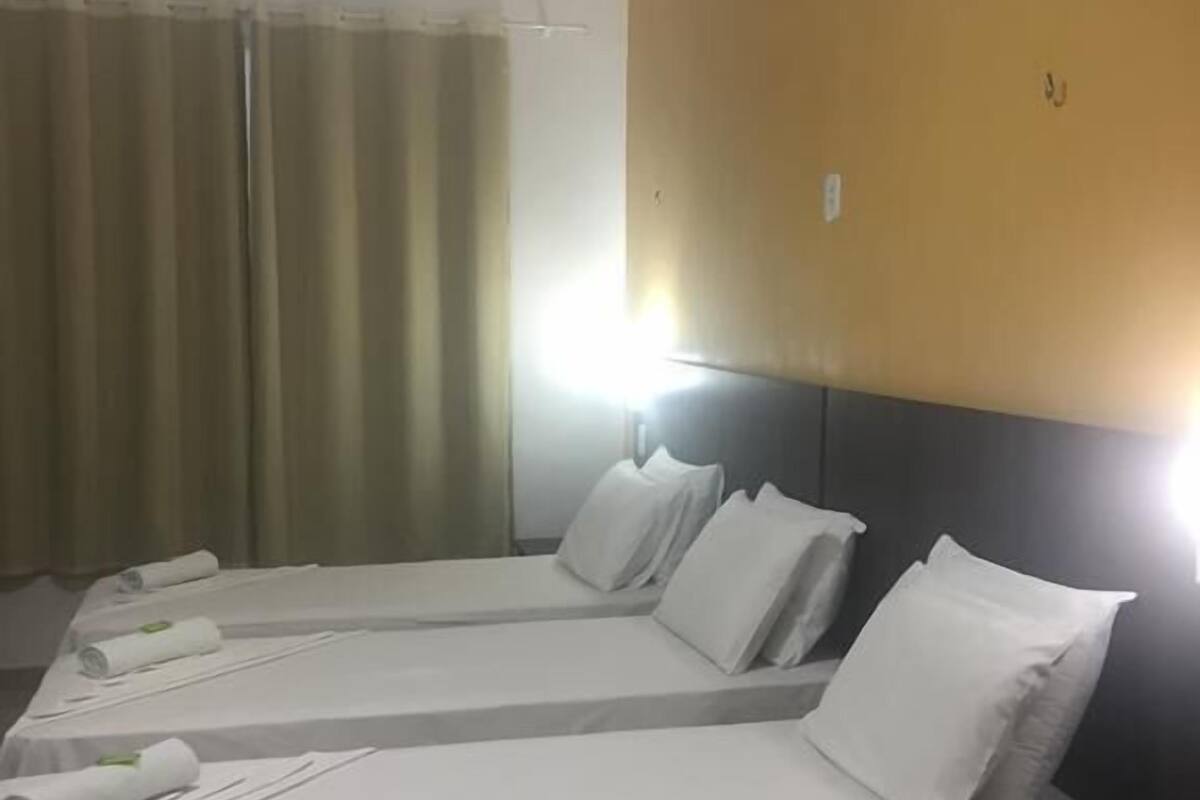 A hotel room with two single beds, each with white linens and pillows, a small bedside table, and a headboard.