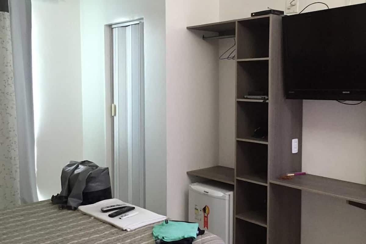 A hotel room with a bed, a wardrobe, a television, and a small refrigerator.