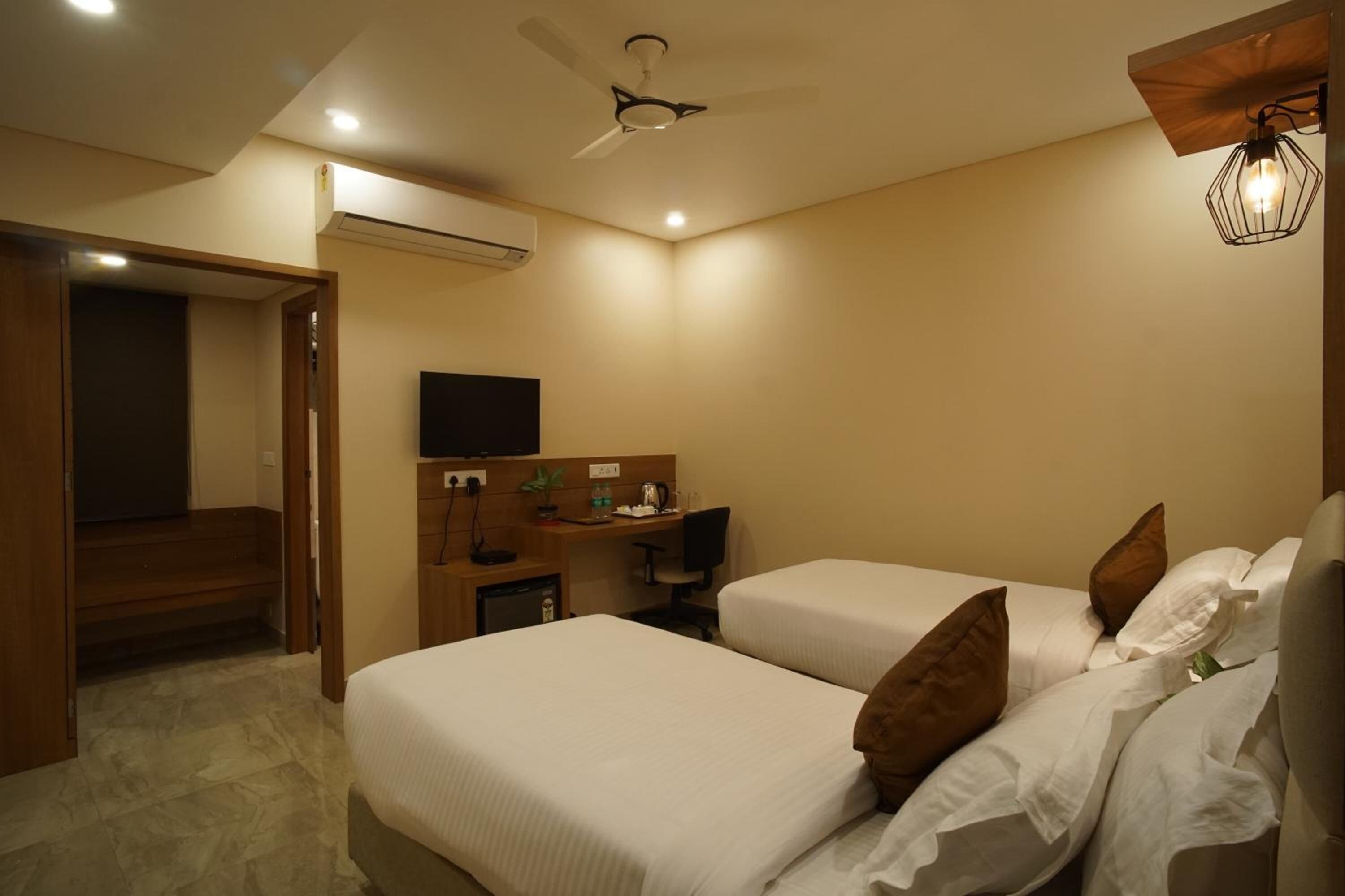 A hotel room with two beds, a desk with a chair, a television, and a ceiling fan.