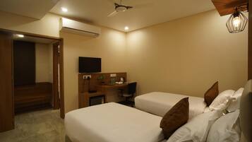 A hotel room with two beds, a desk with a chair, a television, and a ceiling fan.