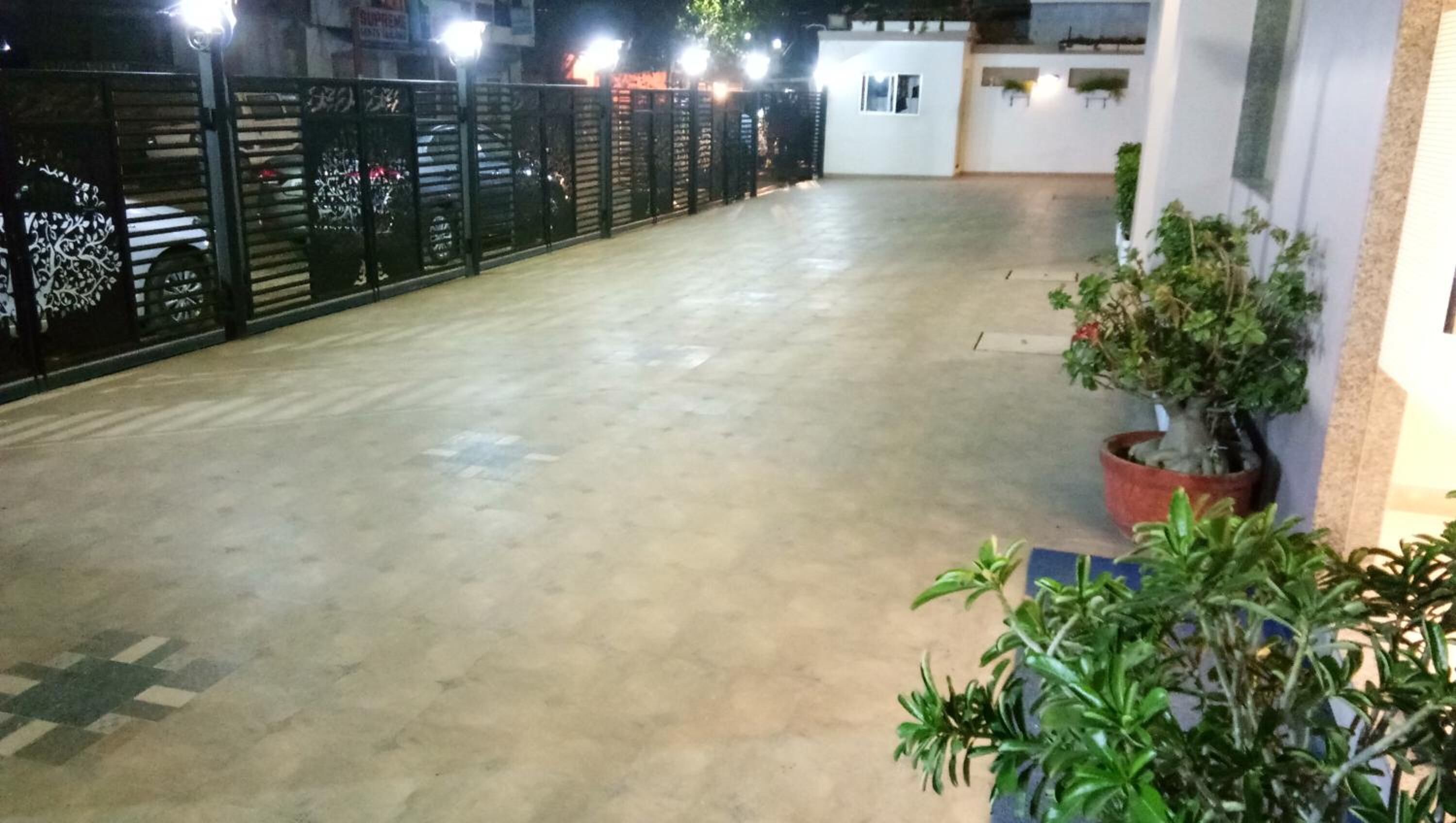 A spacious outdoor area with a concrete floor, a black metal fence, and potted plants.