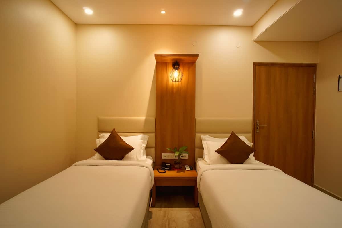 Een hotelkamer met twee bedden, een houten nachtkastje ertussen, een wandlamp en een deur.