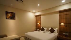 A modern hotel room with a large bed, bedside lamps, a small table, and a painting on the wall. - Hotel Shree Kanha Residency (Prayagraj)