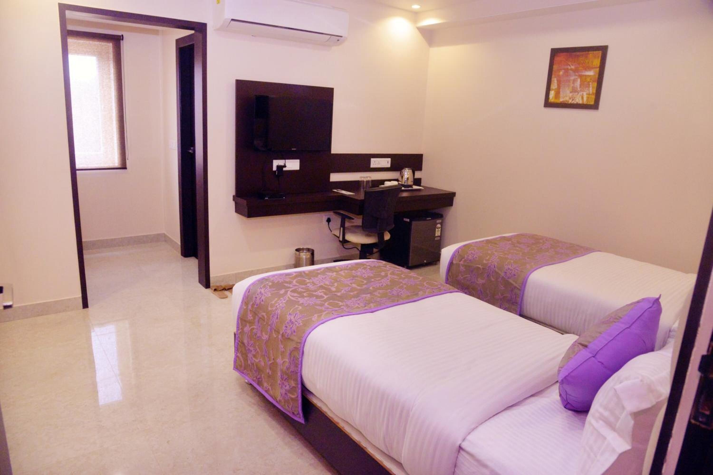 A hotel room with two beds, a desk, a chair, a TV, and a window.