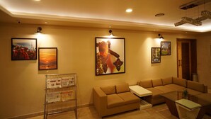 A hotel lobby with a sofa, a coffee table, and wall-mounted artwork. - Hotel Shree Kanha Residency (Prayagraj)