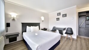 A modern hotel room with a large bed, bedside tables, a desk with two chairs, and a staircase leading to an upper level.