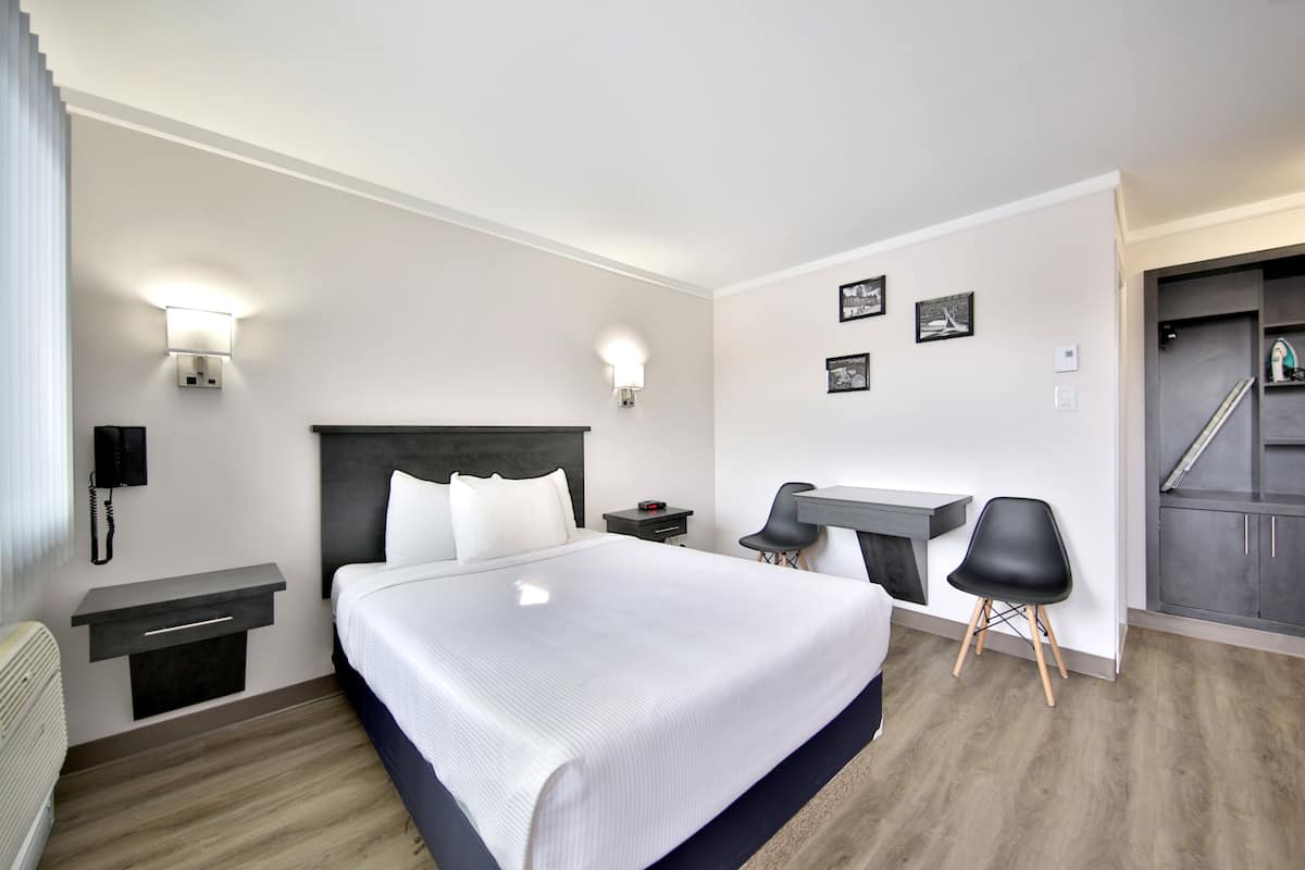 A modern hotel room with a large bed, bedside tables, a desk with two chairs, and a staircase leading to an upper level.