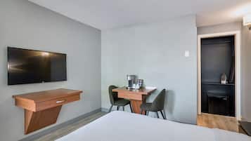 A hotel room with a bed, a desk with chairs, a coffee machine, and a TV mounted on the wall.