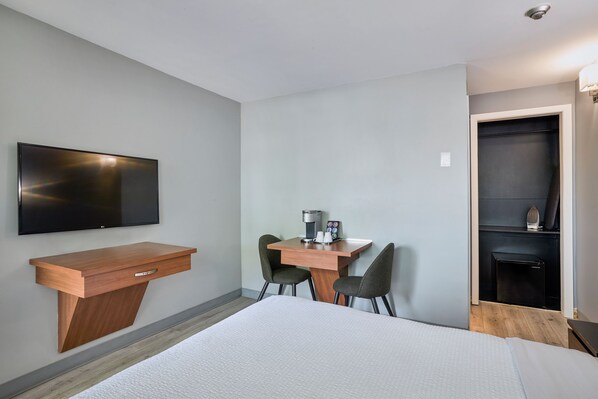 A hotel room with a bed, a desk with chairs, a coffee machine, and a TV mounted on the wall.