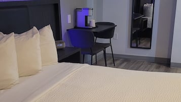 A hotel room with a large bed, a desk with a coffee maker, a chair, and a mirror on the wall.