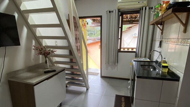 A compact kitchen with a wooden staircase, a small dining area, and a TV mounted on the wall. - Mareou (Angra dos Reis)