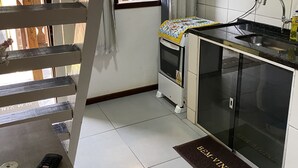 A compact kitchen with a built-in sink, a small window with curtains, and a shelf with kitchen utensils. - Mareou (Angra dos Reis)
