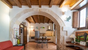 Un intérieur chaleureux, avec une arche en pierre menant à la cuisine, un coin repas avec des chaises et un canapé à rayures rouges.