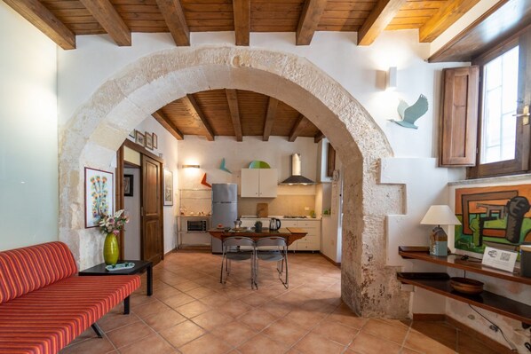 A cozy interior with a stone archway leading to a kitchen, a dining area with chairs, and a red-striped sofa.