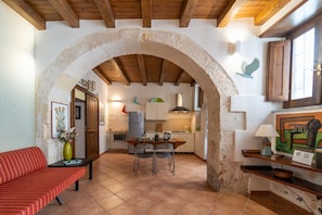 A cozy interior with a stone archway leading to a kitchen, a dining area with chairs, and a red-striped sofa.