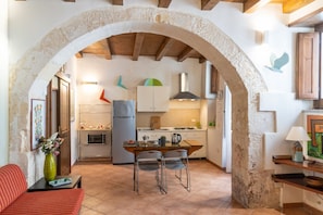 A rustic kitchen with an archway, a dining table with chairs, and a sofa.
