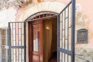 An arched doorway with a wooden door, a metal gate, and a stone wall with a number sign.
