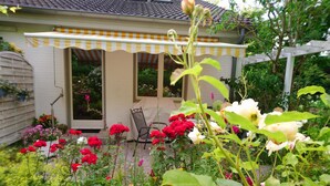A garden with a covered patio area, a chair, and various flowering plants.