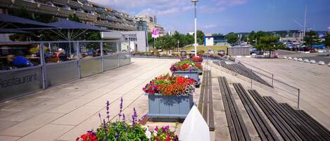 A rooftop terrace with outdoor seating, a modern building with a glass facade, and a clear sky.