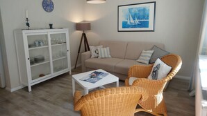 A living room with a sofa, two wicker chairs, a small table, a cabinet, a lamp, a clock, and a framed picture on the wall.