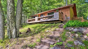 Eine Holzhütte mit Steinfundament, umgeben von Bäumen und einer Steintreppe.