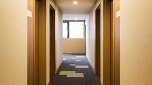 Un pasillo de hotel con piso alfombrado, puertas de madera y una ventana al final.