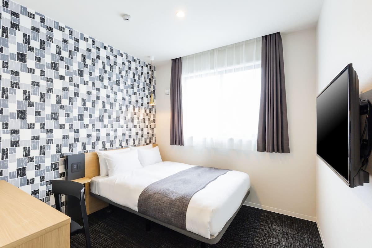 A hotel room with a bed, a desk, a TV, and a patterned wall.
