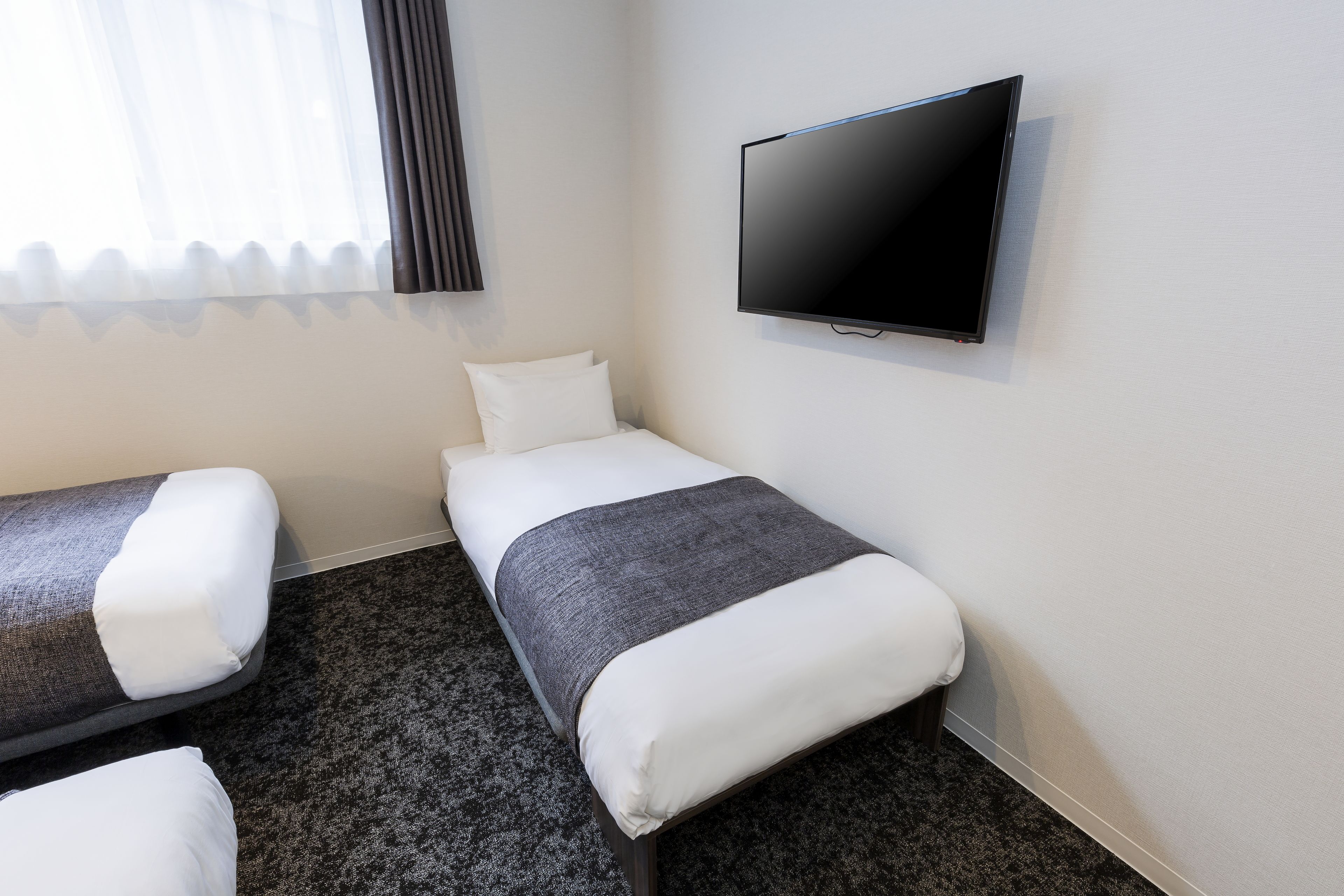 A hotel room with two single beds, a flat-screen TV, and a window with curtains.