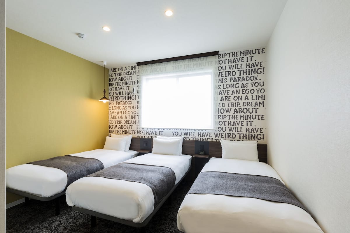 A hotel room with three single beds, a window with curtains, and motivational quotes on the wall.