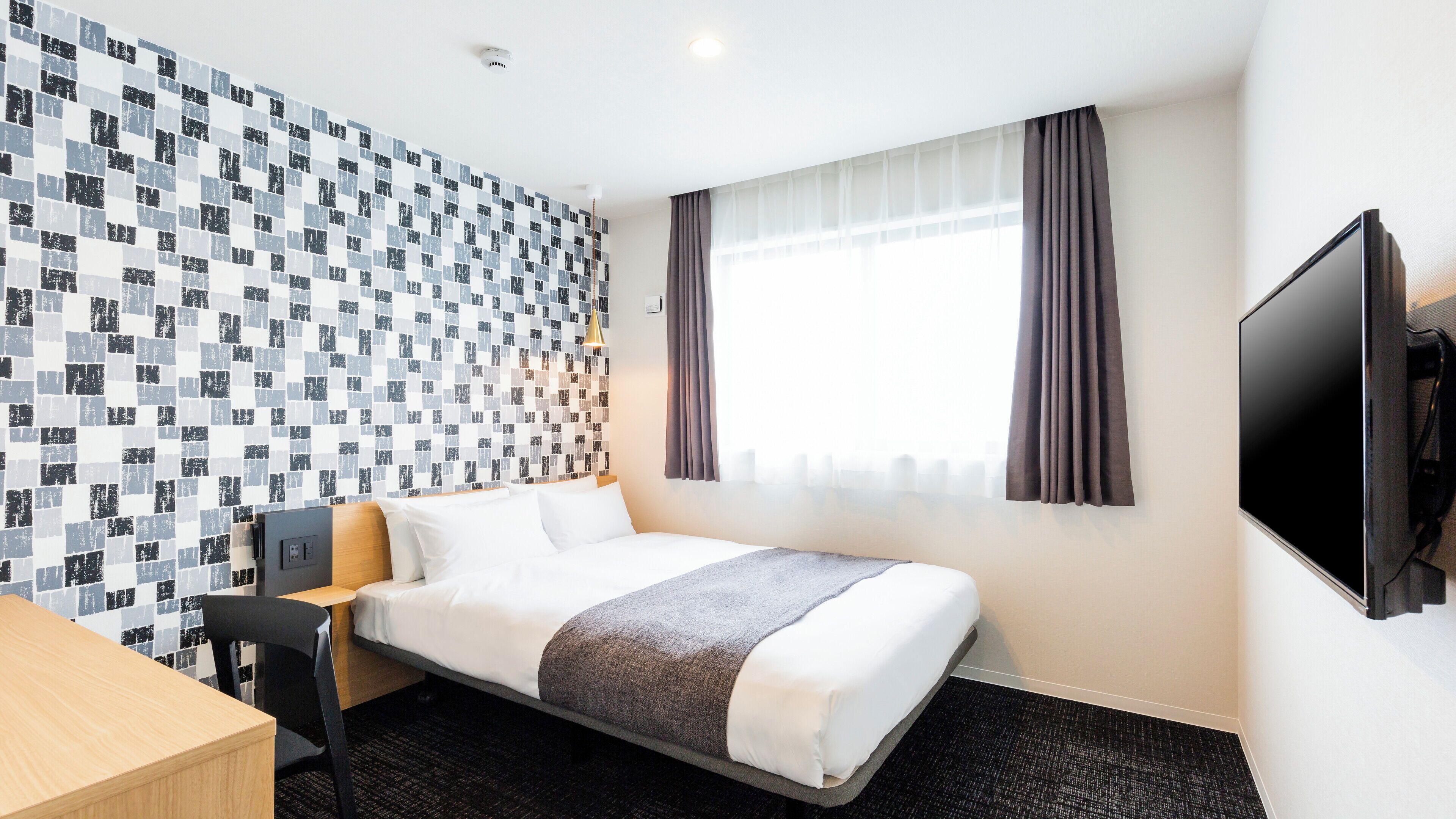 A hotel room with a bed, a desk, a TV, and a window with curtains.