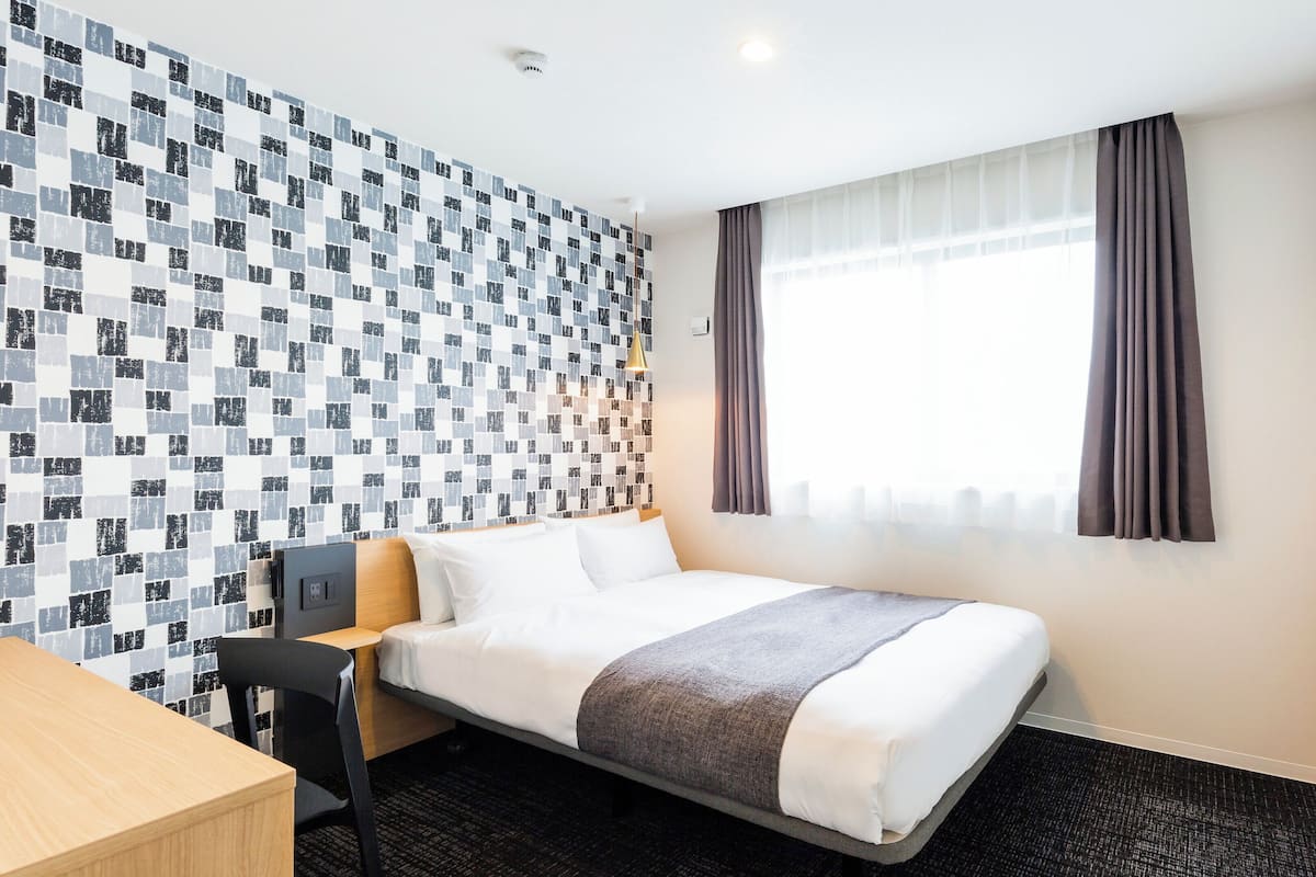 A hotel room with a bed, a desk, a TV, and a window with curtains.