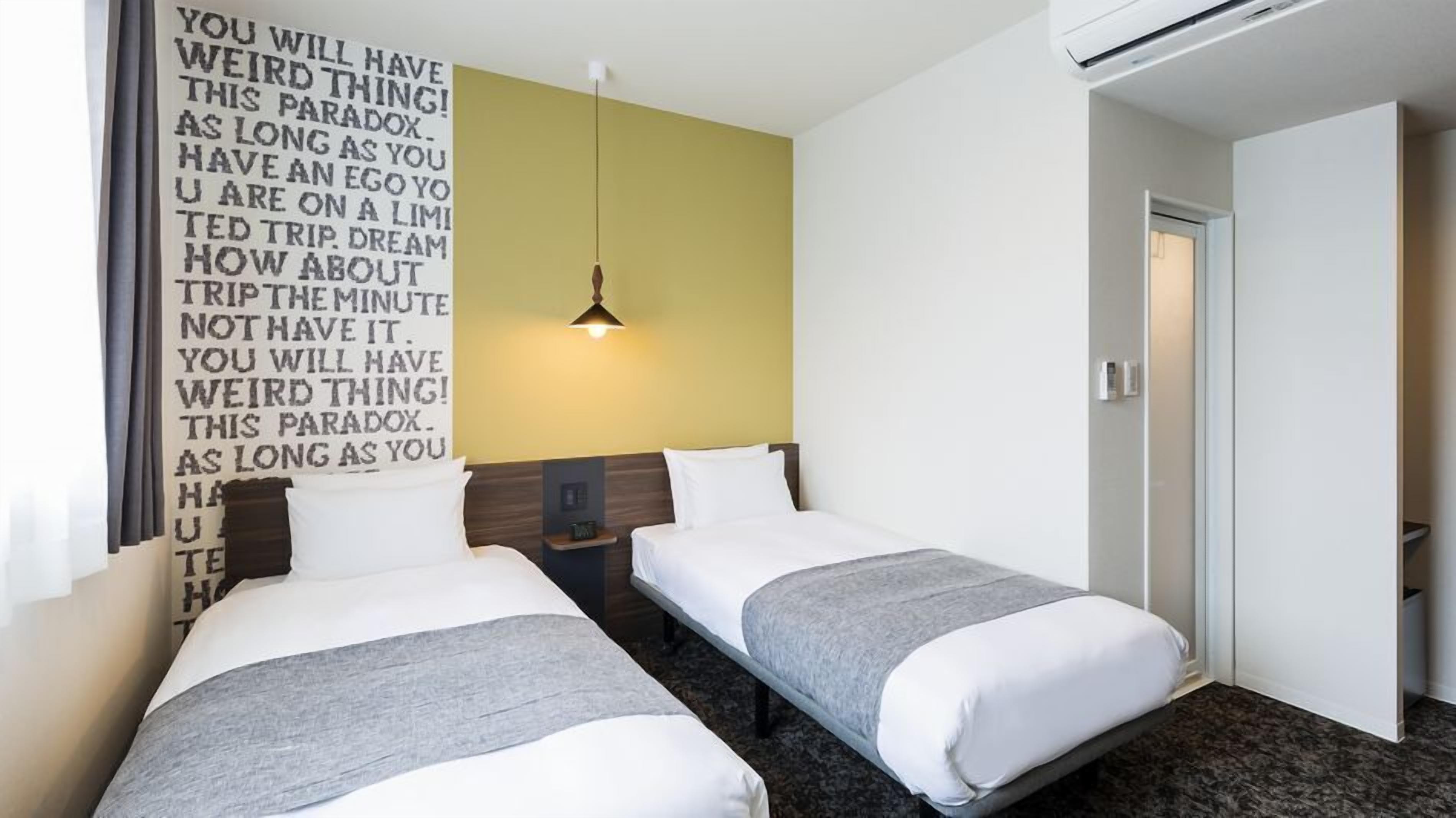 A hotel room with two beds, a wall-mounted light, and a door.