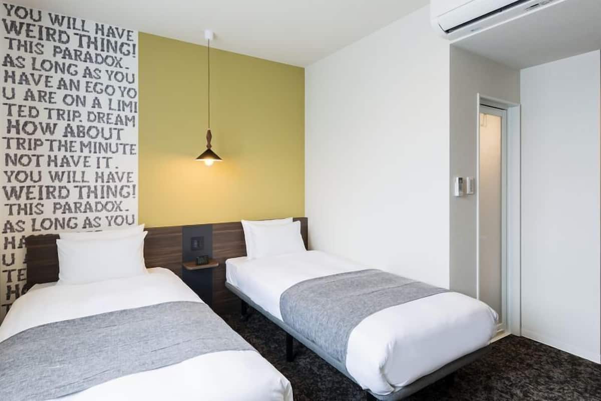 A hotel room with two beds, a wall-mounted light, and a door.