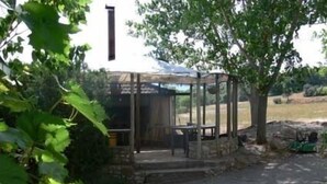 A covered outdoor seating area with stone steps, surrounded by greenery and a white building in the background. - Casa Baltasar, ideal for families and friends, with garden and barbecue. (Isábena)