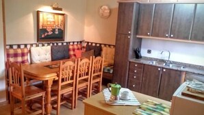 A compact kitchen with wooden cabinets, a dining table with chairs, and a small coffee station. - Casa Baltasar, ideal for families and friends, with garden and barbecue. (Isábena)