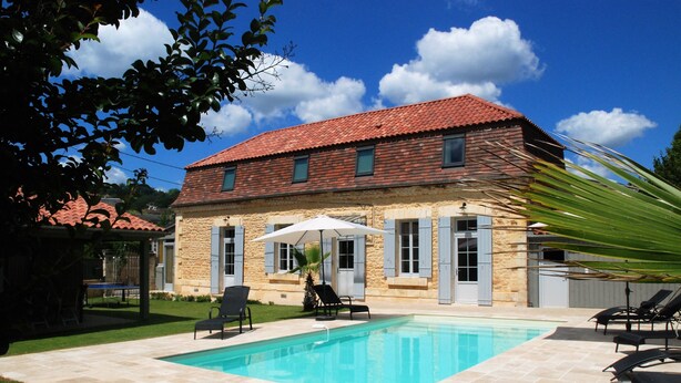 Una casa con piscina, paredes de piedra y techo de tejas rojas.